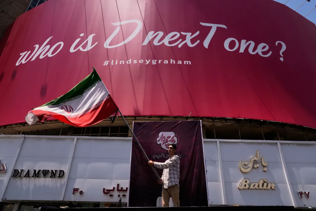 A man waves an Iranian flag in front of a billboard that reads,