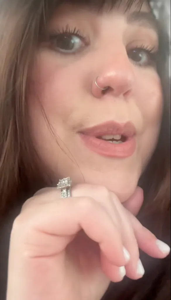 A close-up of a woman's face from the nose down, wearing a nose ring and a diamond ring on her left hand.