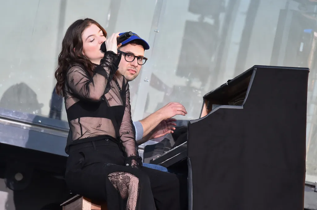 Lorde singing into a microphone while Jack Antonoff plays the piano.