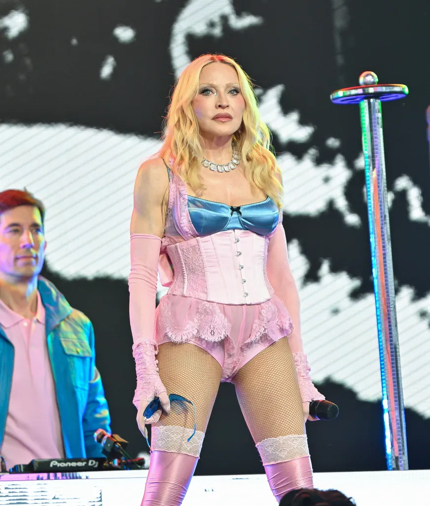 Madonna performing in a pink and blue corset, fishnet stockings, and pink boots on stage.
