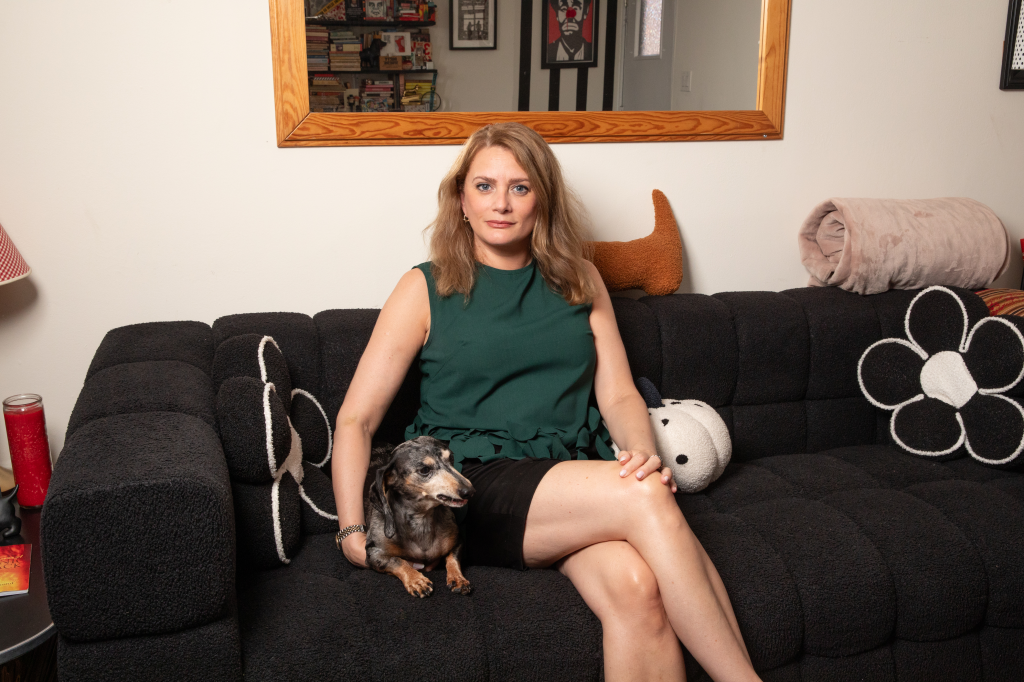 Manhattan real estate publicist Kelly Kreth sits in a green dress with her dachshund on a couch.
