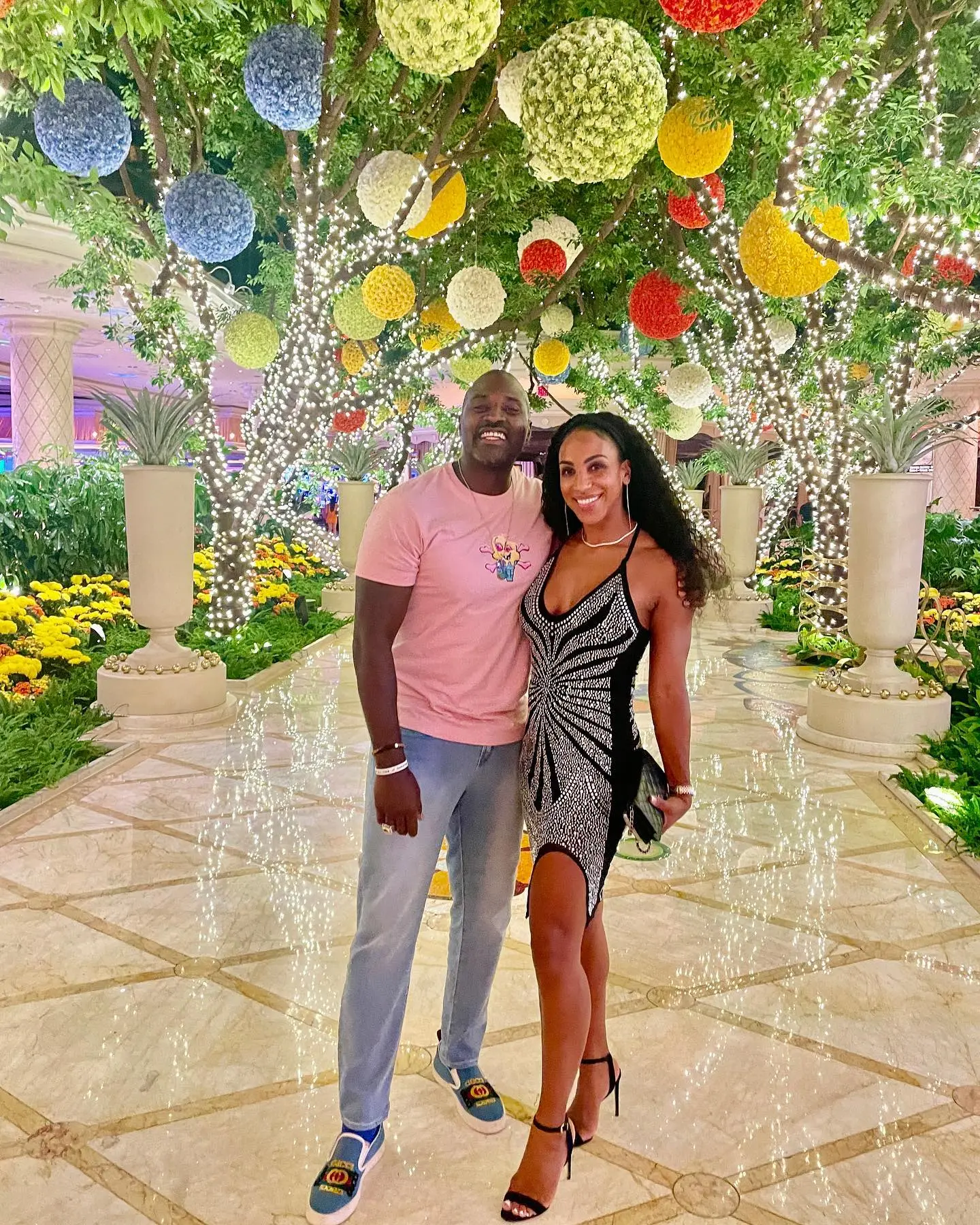 Marcellus Wiley and Annemarie Wiley posing under illuminated trees adorned with decorative orbs.