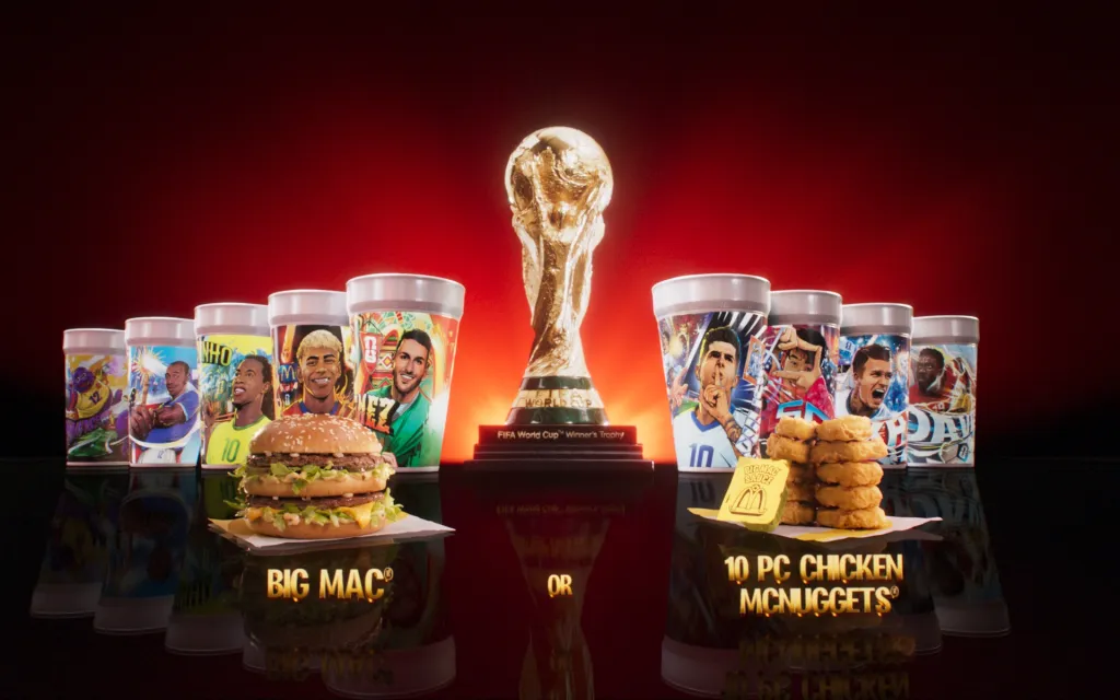 McDonald's FIFA World Cup limited-time meals featuring a Big Mac, 10-piece Chicken McNuggets with Big Mac sauce, and collectible cups with images of soccer players, all centered around a FIFA World Cup trophy.