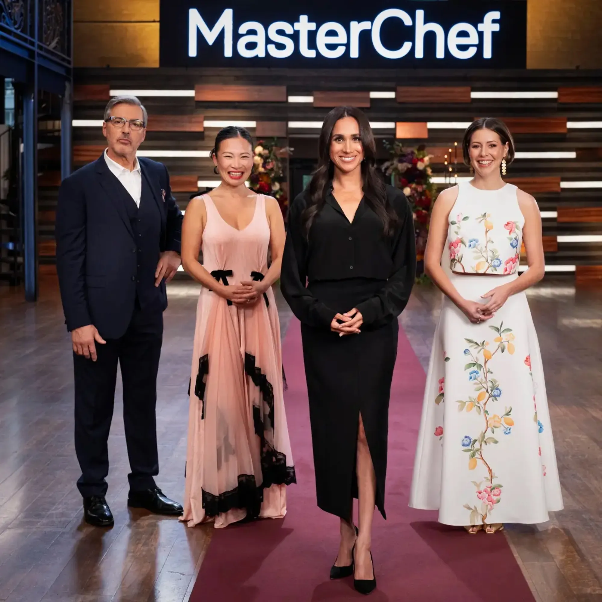 Meghan Markle and three other people pose for a photo in front of a 