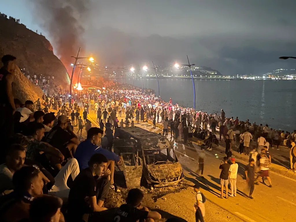 Migrants gather around a torched vehicle while waiting for a chance to cross to the Spanish enclave of Ceuta, on the Moroccan side of the border in Fnideq, Morocco, July 31, 2026.