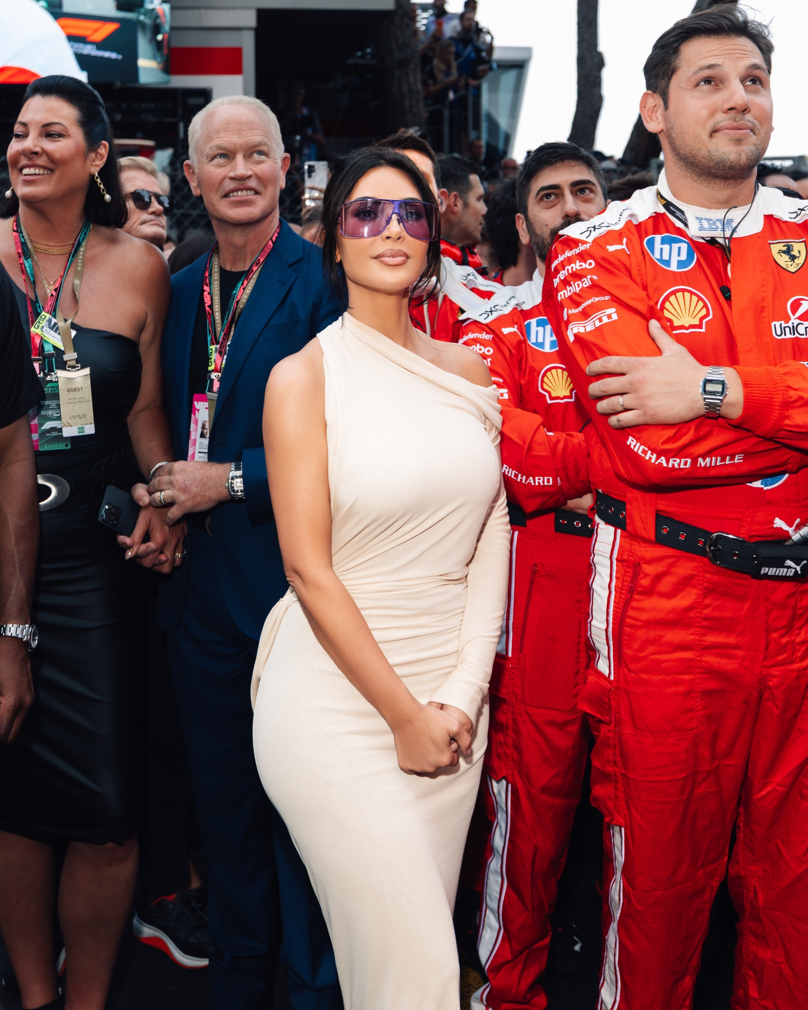 Kim Kardashian, wearing a beige dress and purple visor sunglasses, standing among a crowd at the Formula 1 Grand Prix in Monaco.