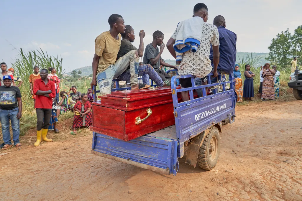 People transporting a red casket in the back of a blue truck.