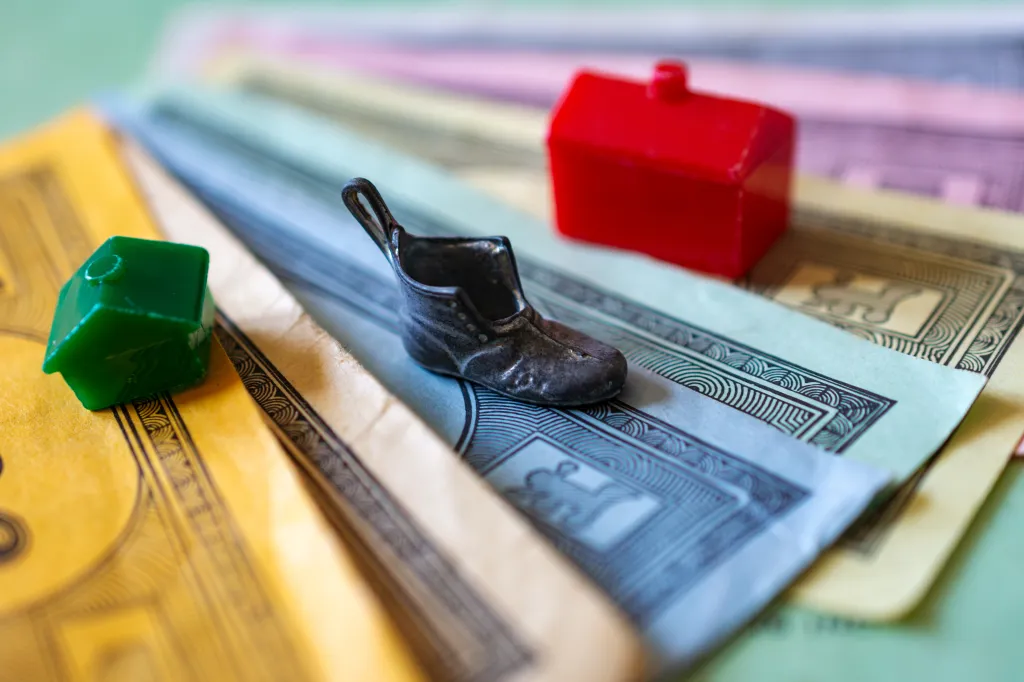 A Monopoly shoe game marker sits on top of Monopoly money with a green house and a red hotel in the background.