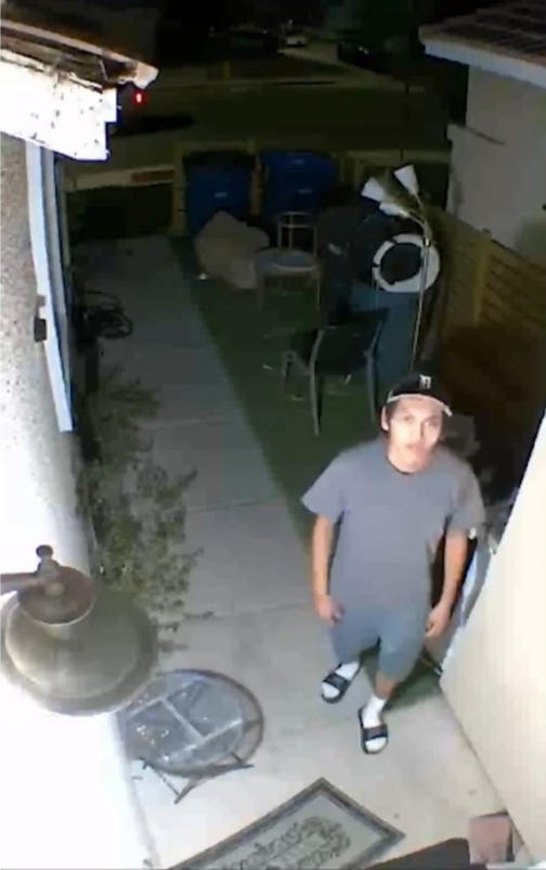 A man in a t-shirt, shorts, and backward cap looks up at a camera.
