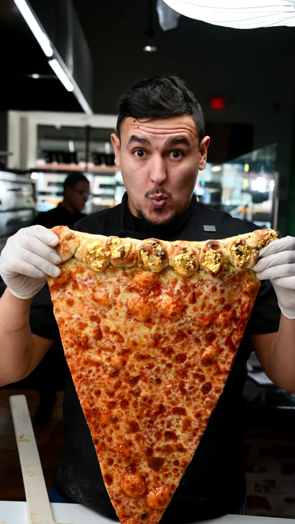 Chef Joe Brignoni holding a pizza slice with a garlic knot crust topped with edible gold leaf.