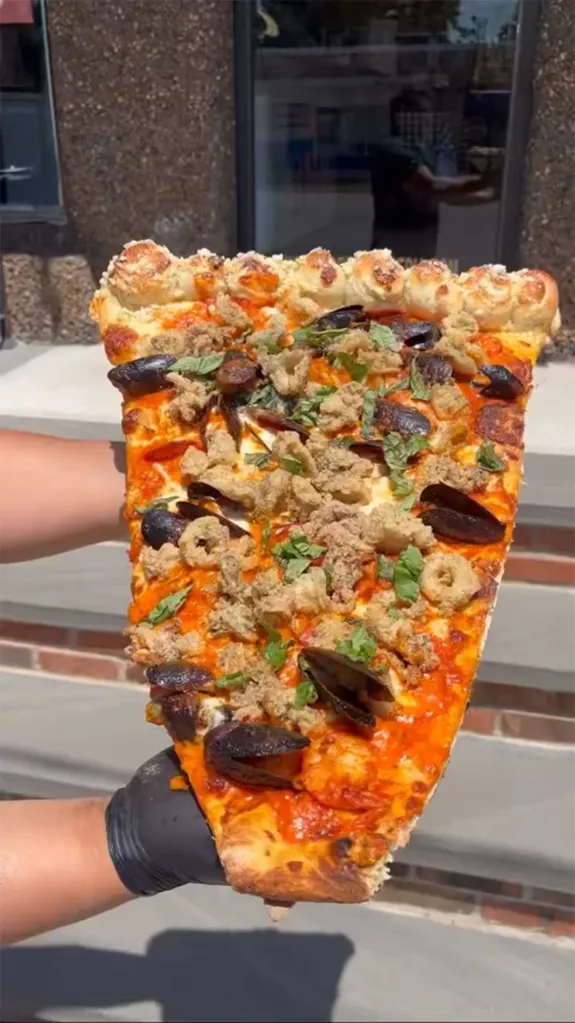 A large slice of seafood fra diavolo pizza with mussels, fried calamari, and shrimp, served on a garlic knots crust.
