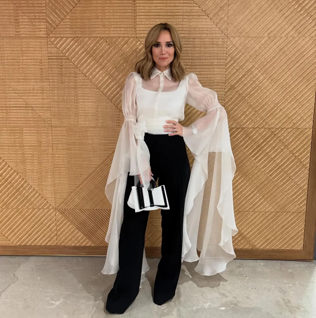Sara Gore in a sheer white blouse with dramatic sleeves and black pants.