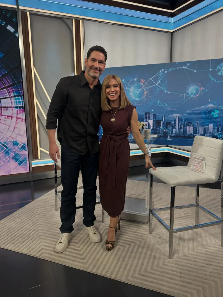 Sara Gore and Tom Ellis posing on a news set.