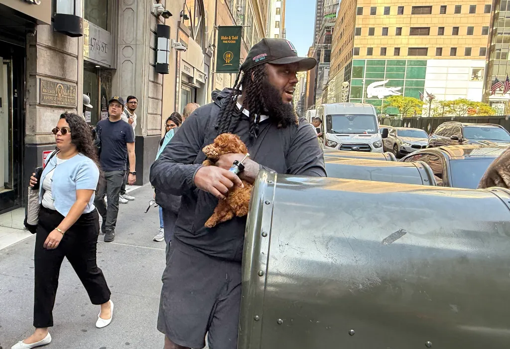 A man holds a small brown puppy as he stands next to a metal stroller on a city street.