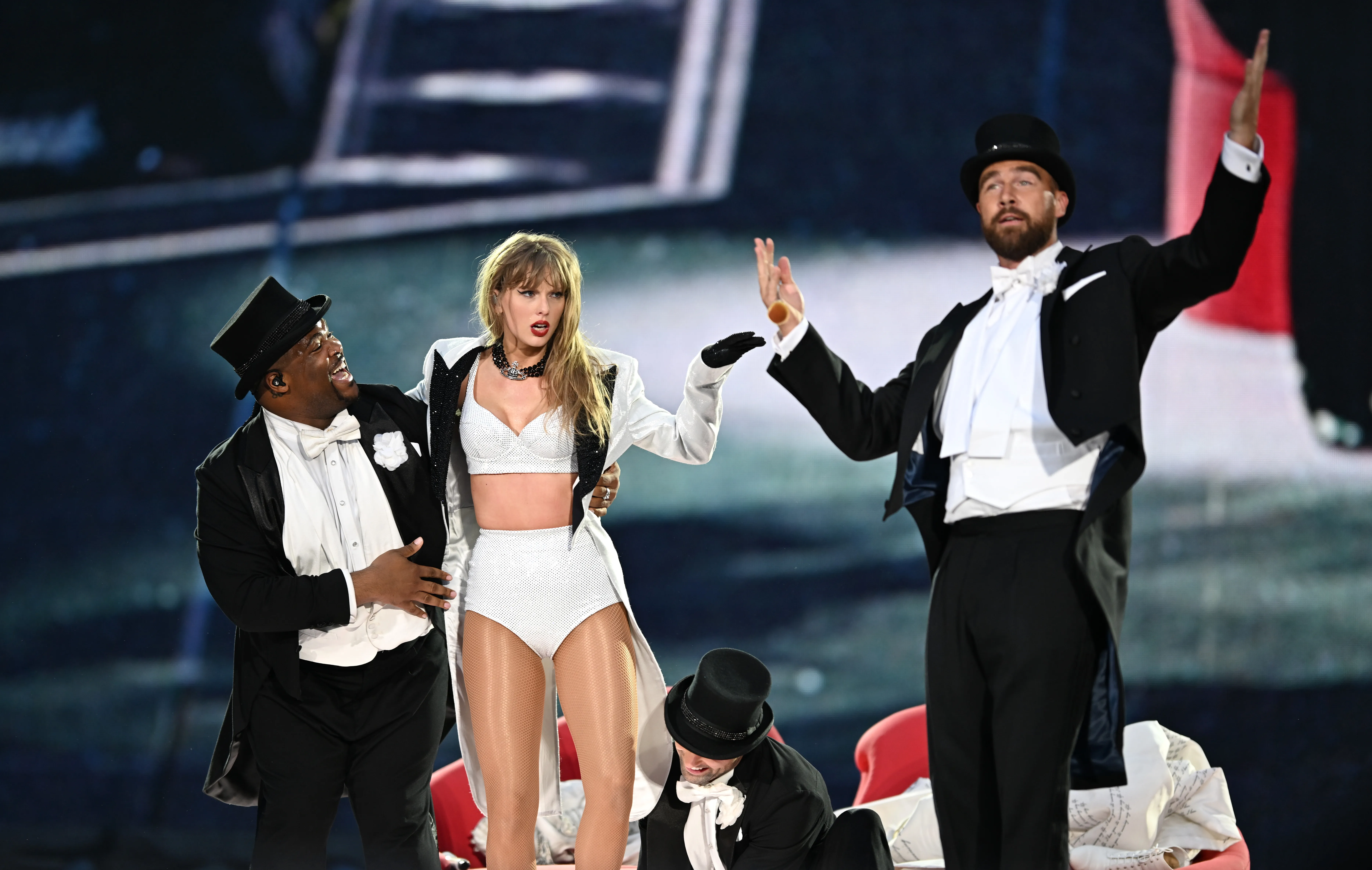 Taylor Swift onstage with Travis Kelce, who is wearing a top hat and tails.