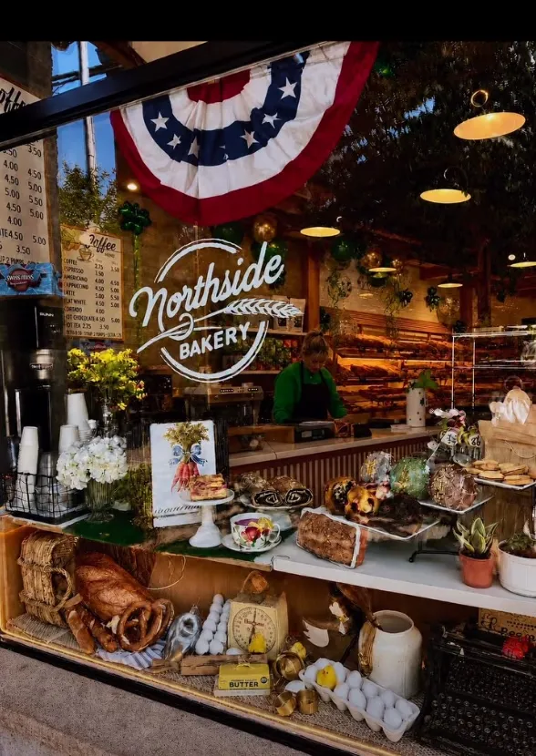 The storefront window of Northside Bakery, featuring pastries, coffee menu, and a baker inside.