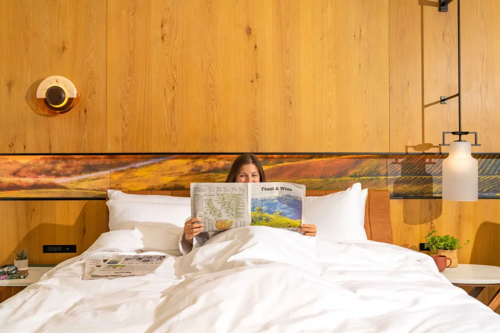 A person reading a newspaper in bed at the Appellation Healdsburg hotel.