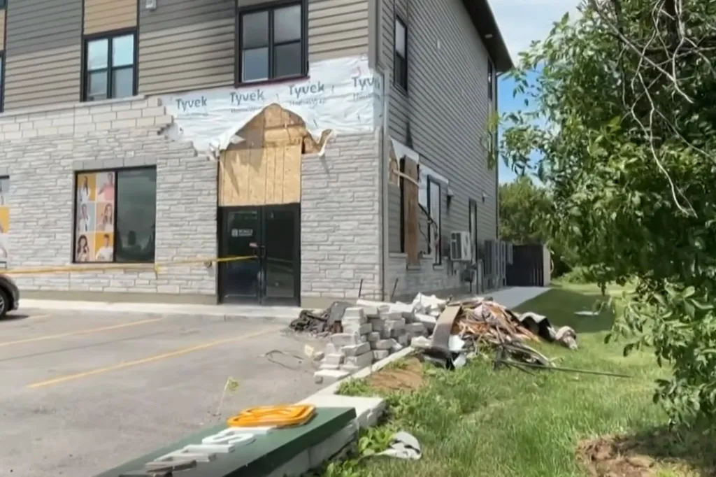 The exterior of a building shows damage to its facade and debris on the ground, with yellow caution tape across the entrance.