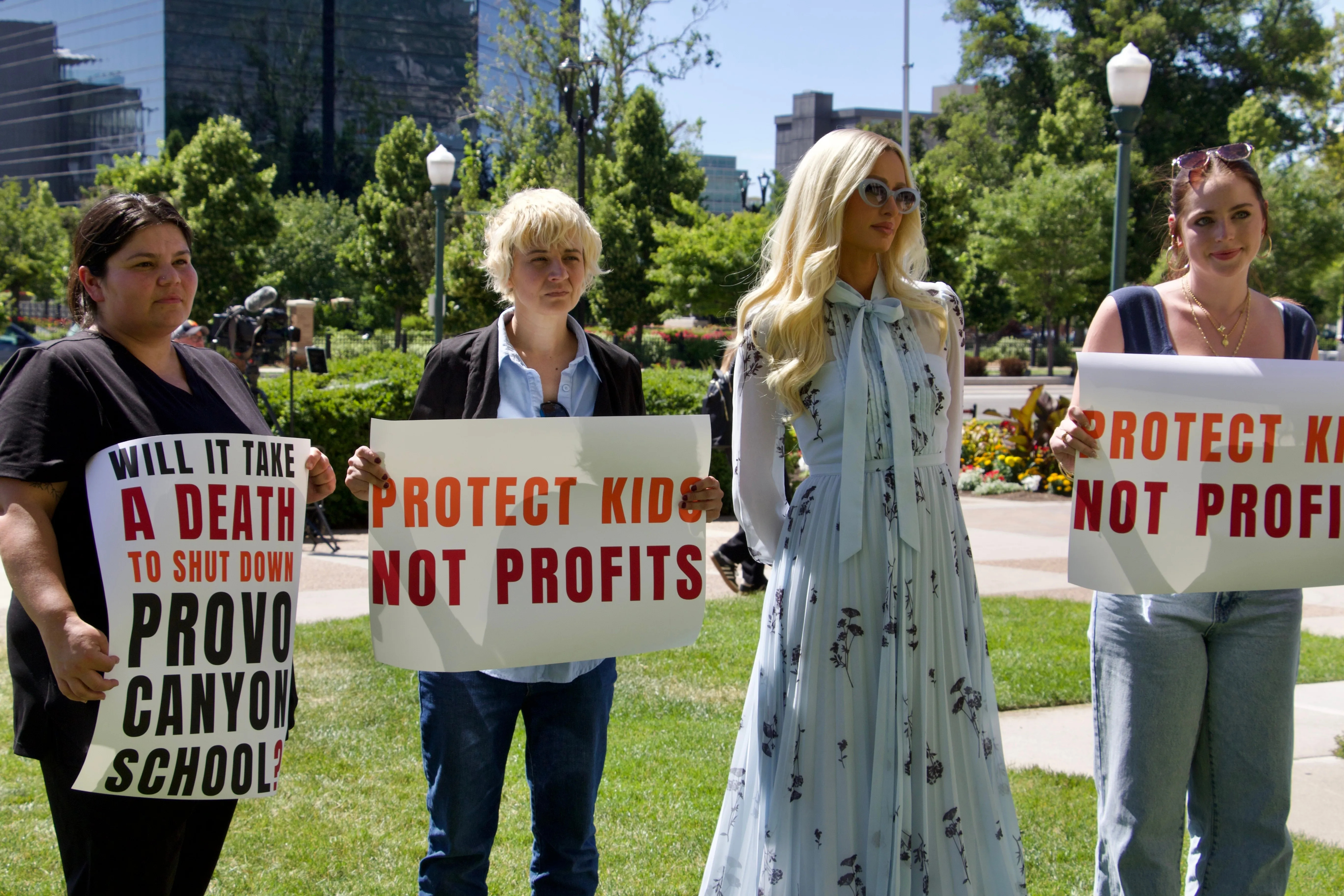 Paris Hilton with fellow survivors of residential teen treatment facilities holding signs that read 