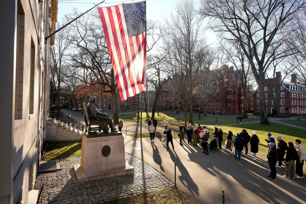 People take photos near a John Harvard statue, left, on the Harvard University campus, Jan. 2, 2024, in Cambridge, Mass.