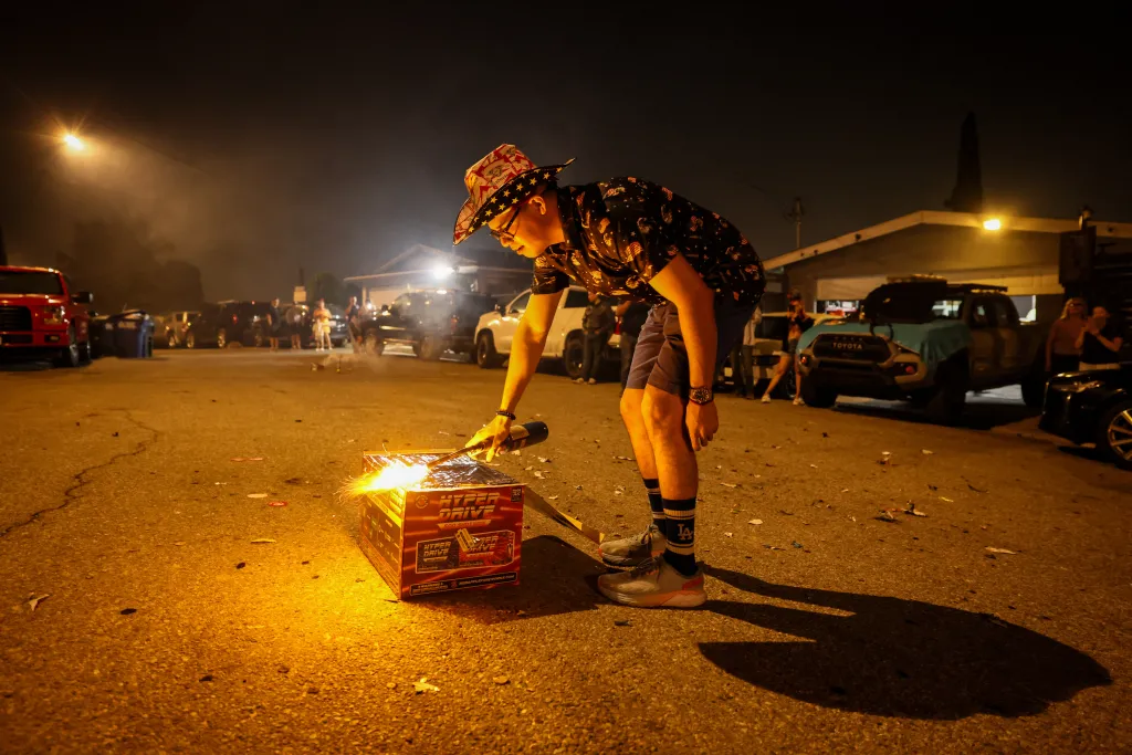 A person in a patriotic hat lights fireworks on a street at night.