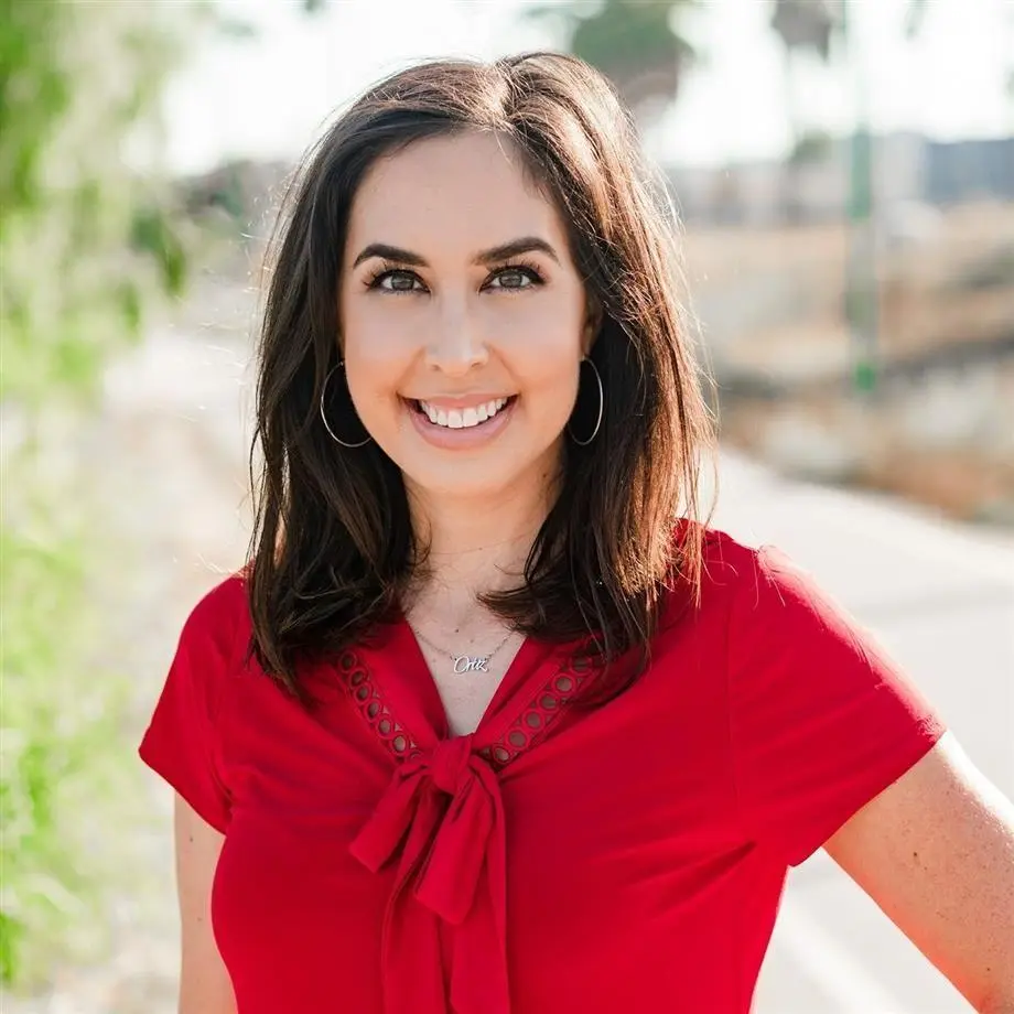 Tanya Ortiz Franklin smiling outdoors, wearing a red shirt and a necklace that reads