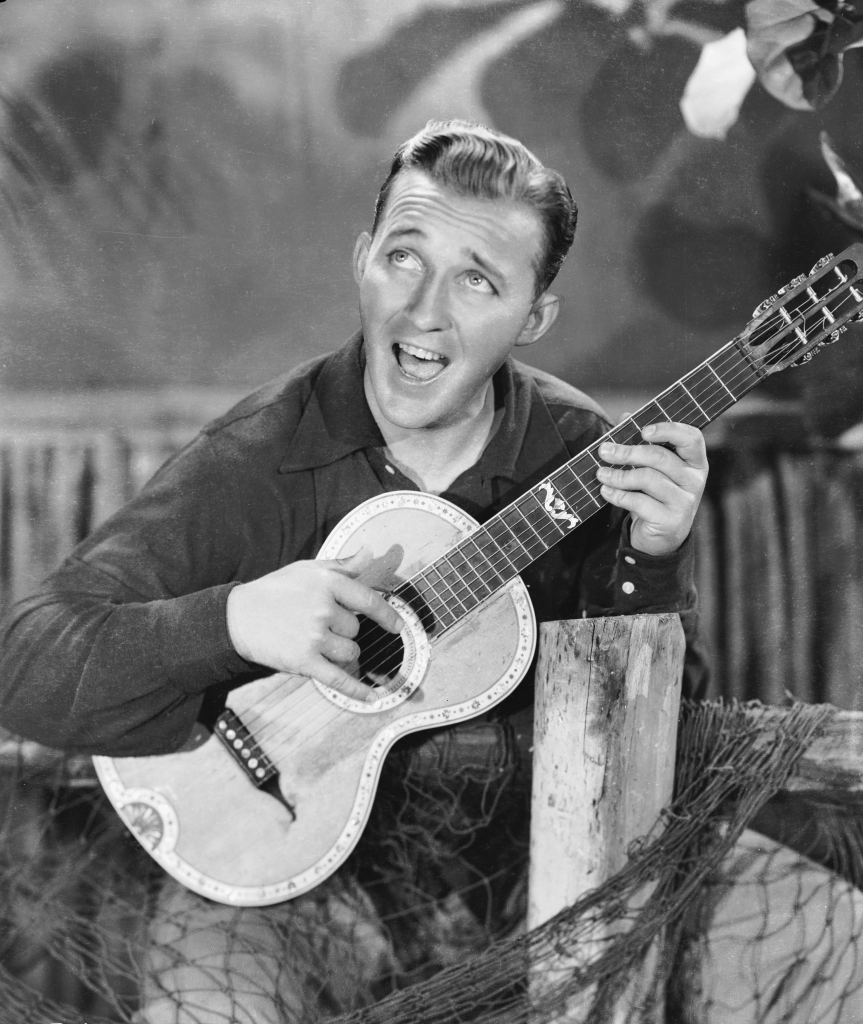 Black and white photo of Bing Crosby playing a guitar and singing.