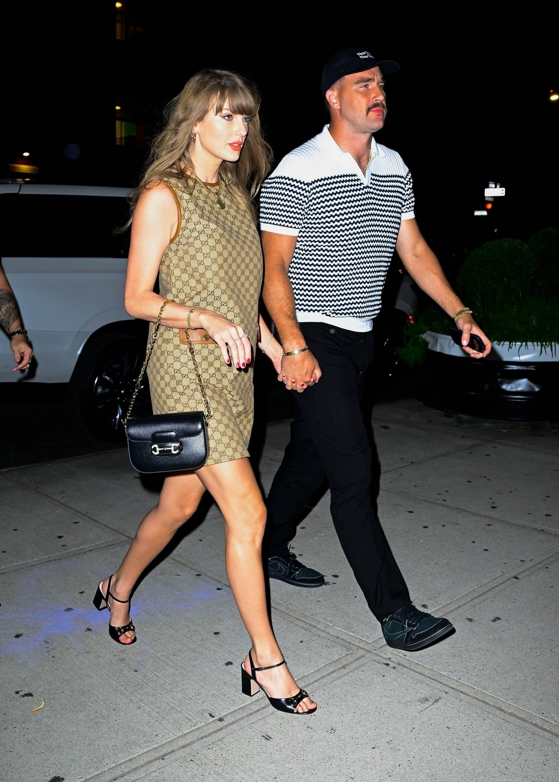 Taylor Swift and Travis Kelce walking hand-in-hand at night.