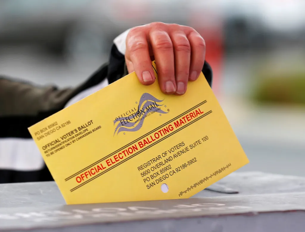 A poll worker places a yellow mail-in ballot into a voting box.
