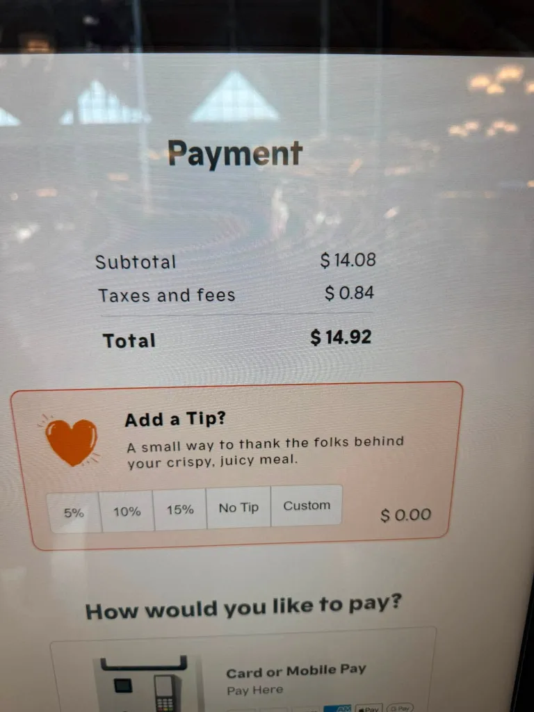 A Popeyes kiosk display shows a payment screen asking for a tip for a $14.92 order.