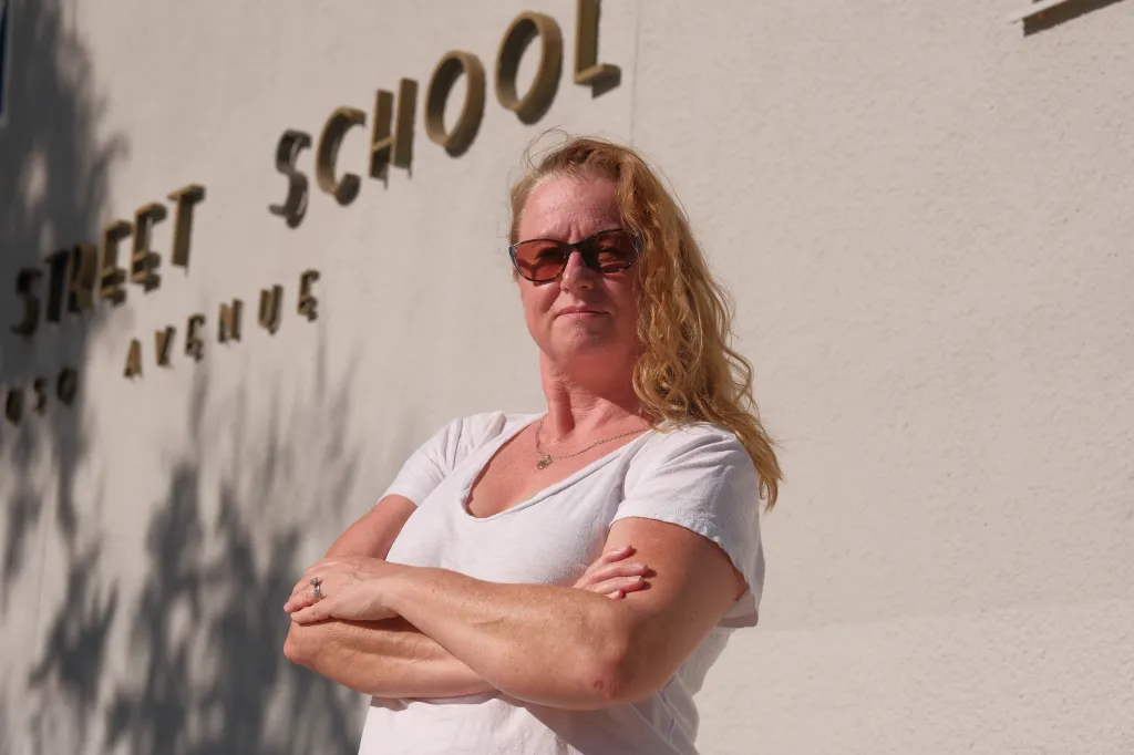 Portrait of Sonia Reiter, 48, with red hair and sunglasses, standing with arms crossed in front of a building with the words