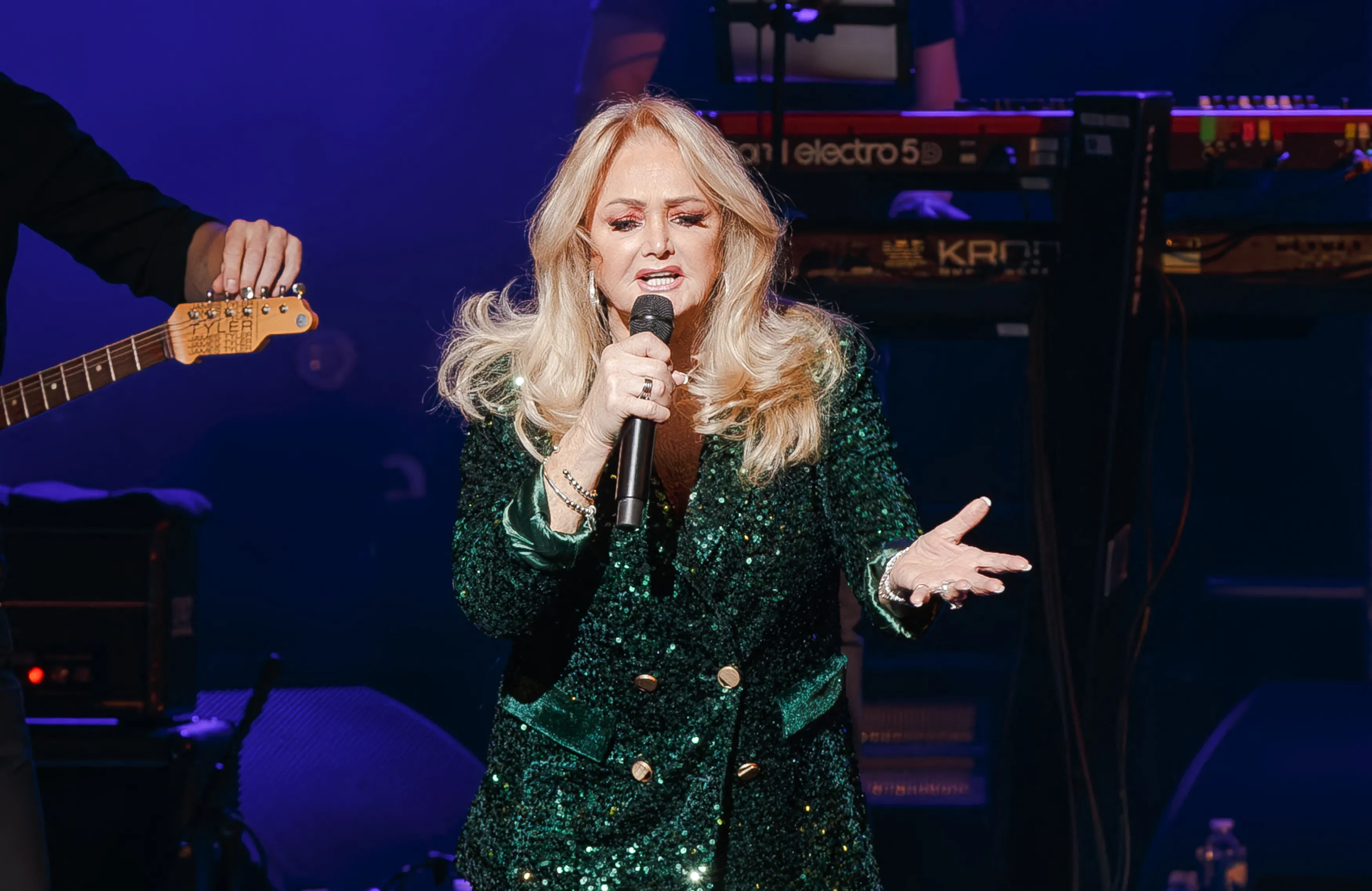 Bonnie Tyler performing on stage in a green sequined jacket.