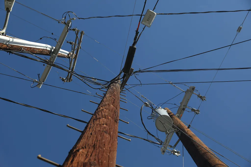 View from below of three wooden power poles and numerous electrical wires against a clear blue sky.