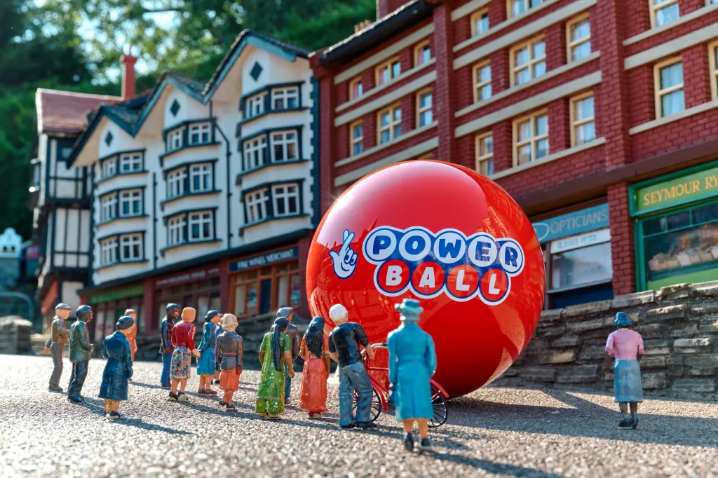 Miniature figures standing in front of a giant red Powerball lottery ball in a model village.