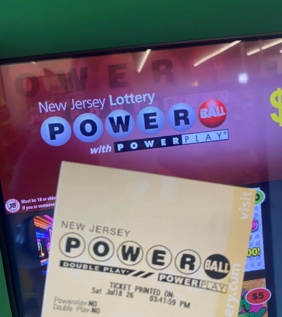 A Powerball lottery ticket in front of a digital screen showing the New Jersey Lottery Powerball logo.
