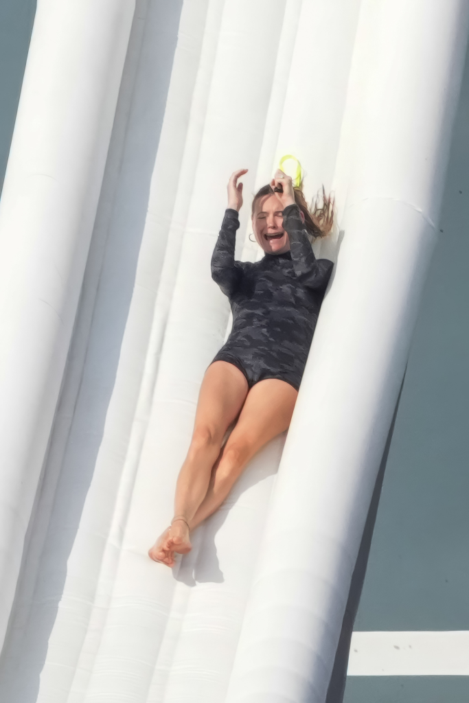 Behati Prinsloo sliding down a slippery white inflatable slide into the water.