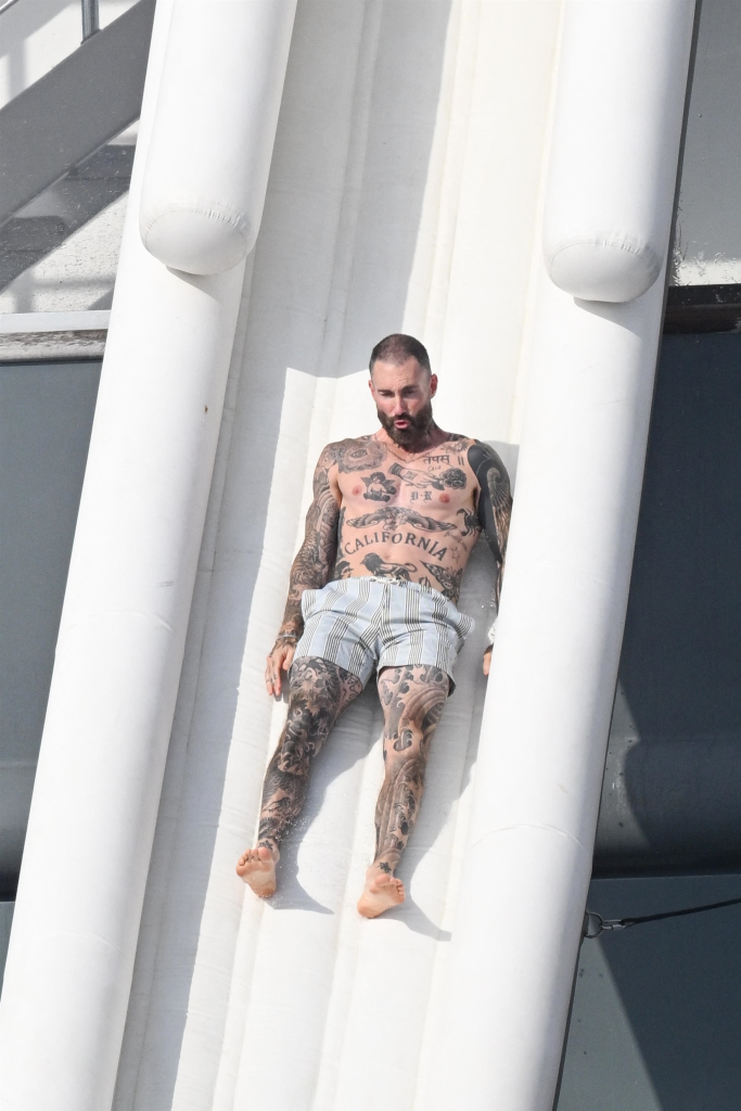 Adam Levine going down a white inflatable water slide on a yacht.