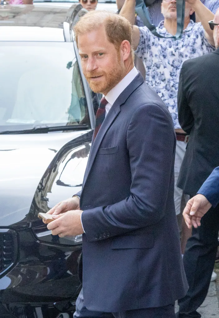Prince Harry in a navy blue suit, exiting Chatham House in London after an Invictus Games event.