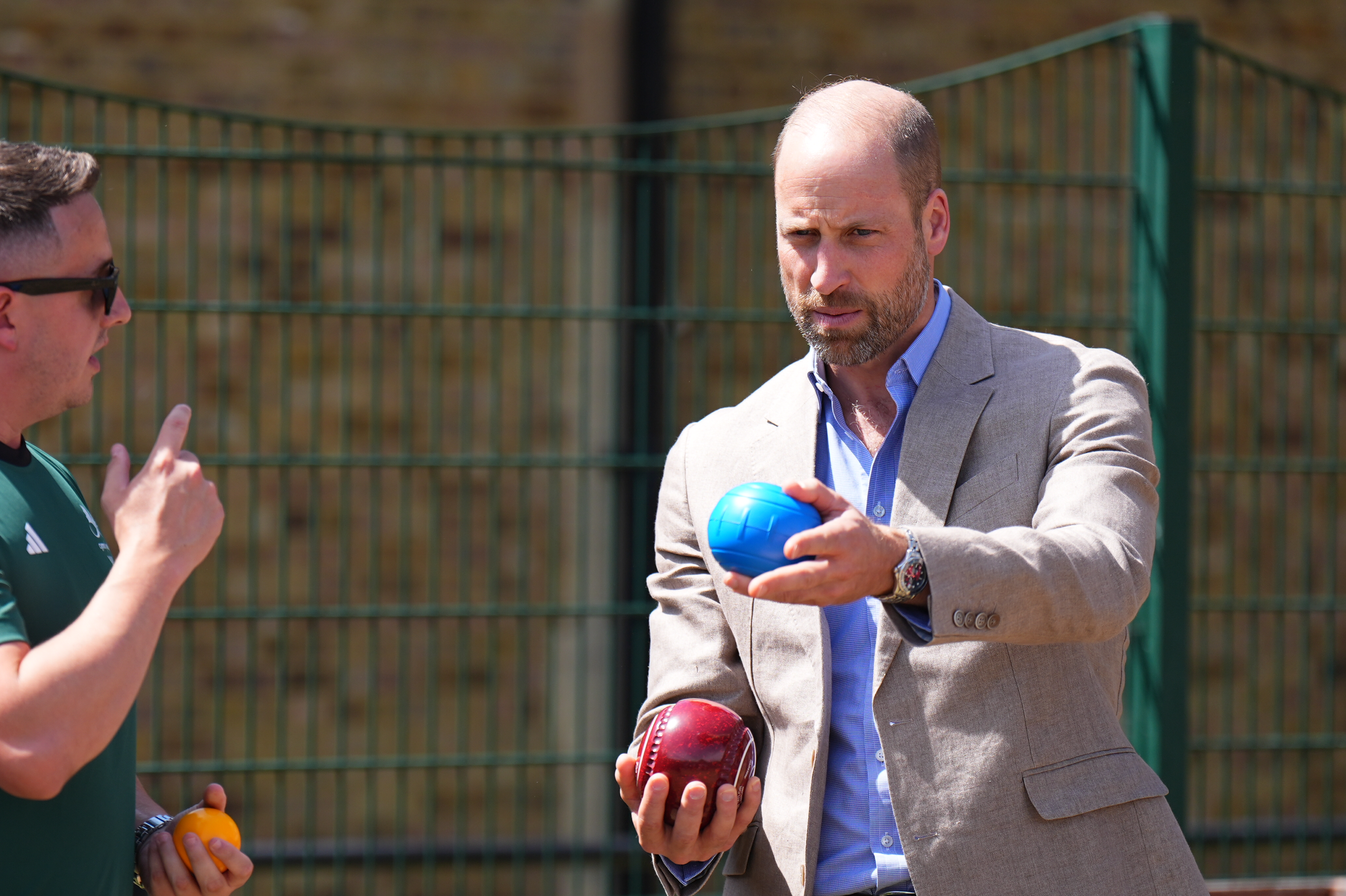 Prince William holding a blue children's bowls ball and a red professional bowls ball.