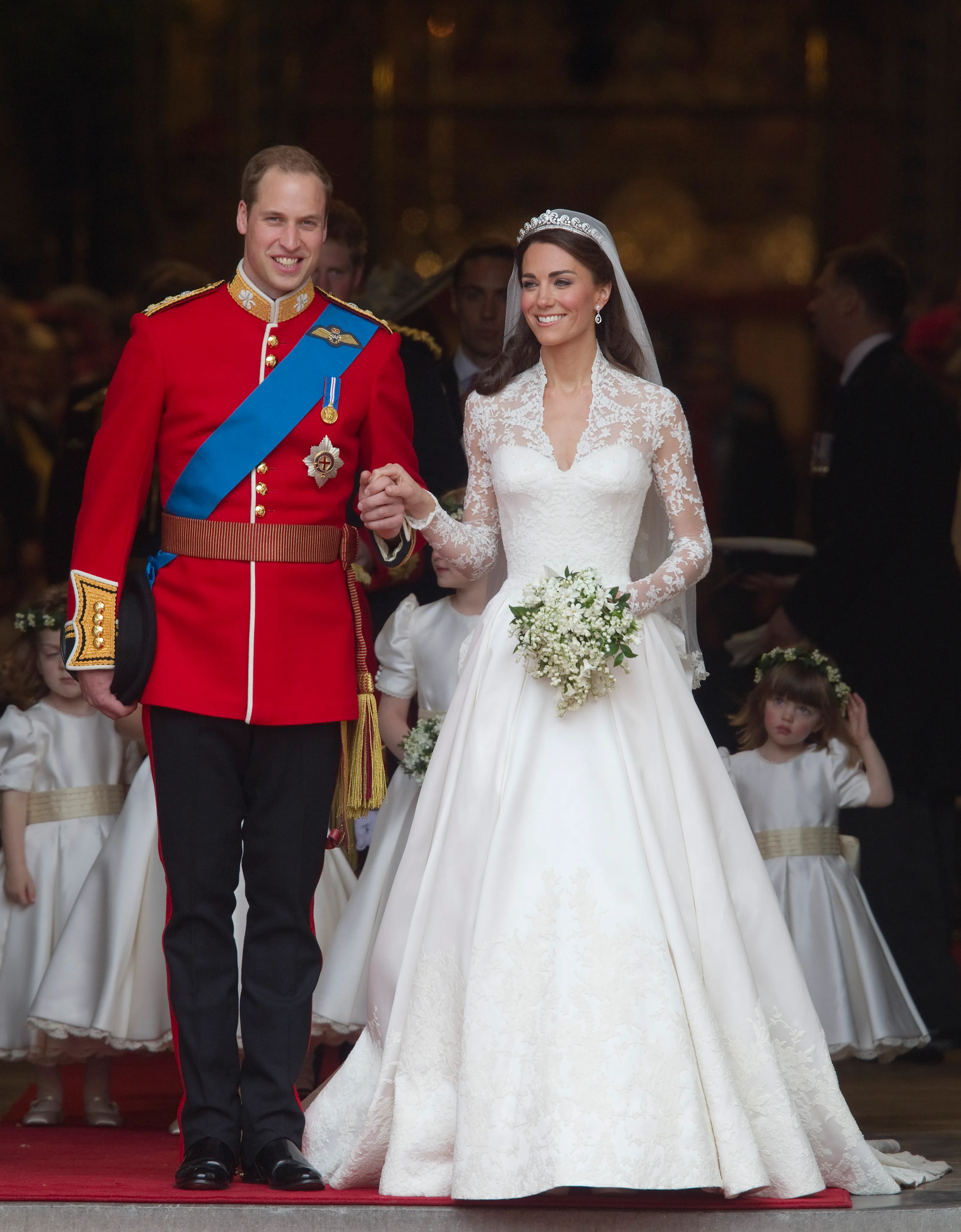 Prince William in military uniform and Catherine Middleton in a white wedding gown holding hands, exiting Westminster Abbey.