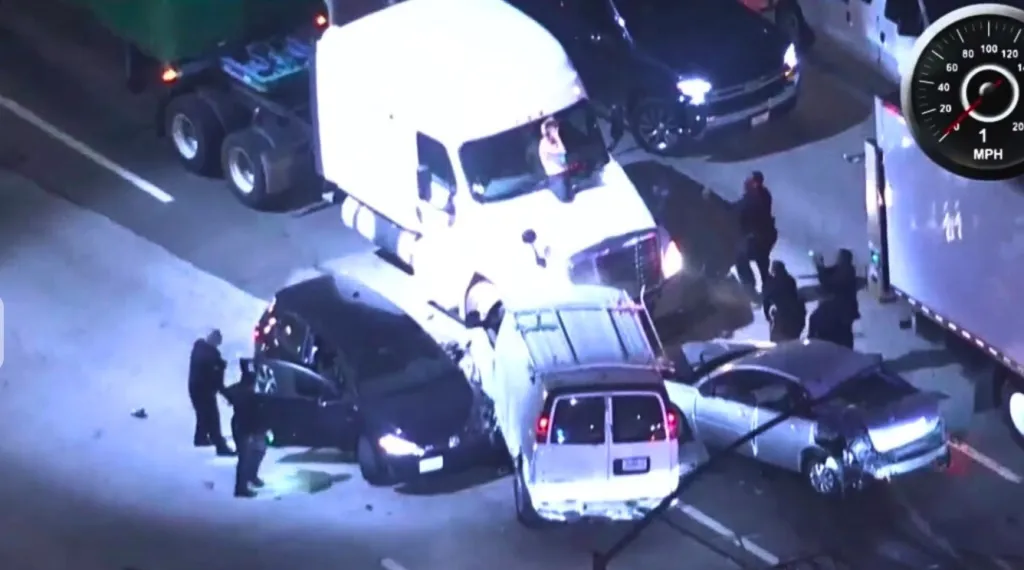 An aerial view of a pursuit ending in a multi-vehicle crash on the 405 Freeway in Santa Monica, with several cars damaged and police surrounding a semi-truck.