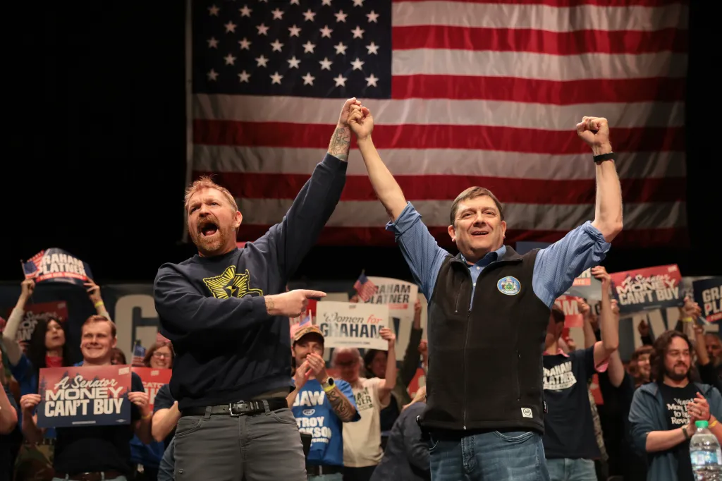 Democratic U.S. Senate candidate Graham Platner and Maine gubernatorial candidate Troy Jackson raise their arms in triumph before an American flag.