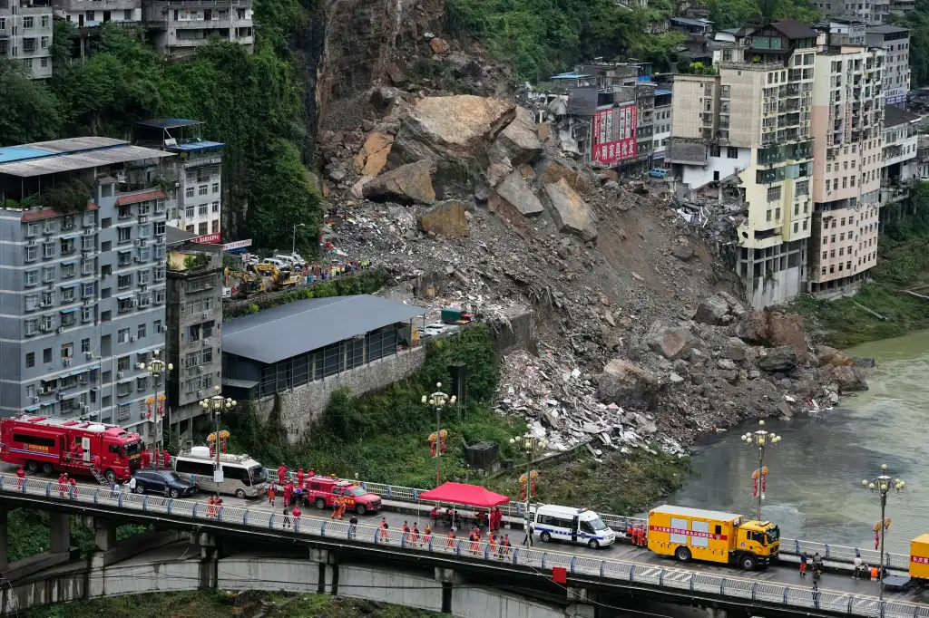 Rescuers prepare on a bridge near a landslide in Pengshui County, China, with debris visible at the base of the mountain and a river below.