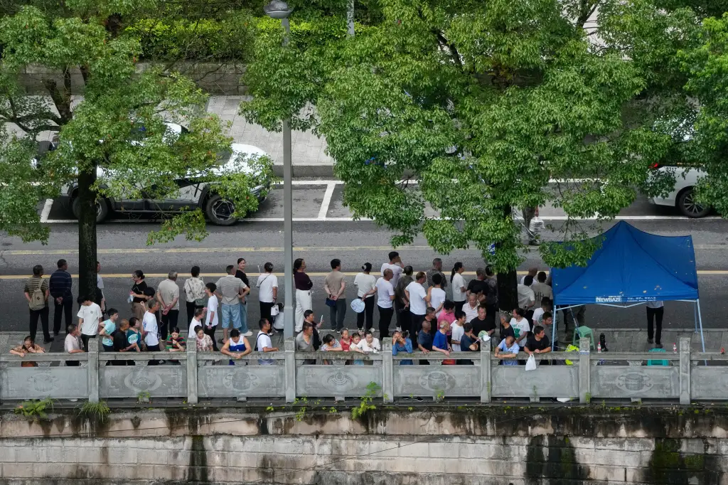 Residents gather at a roadblock to watch rescuers conduct a search and rescue operation following a landslide.