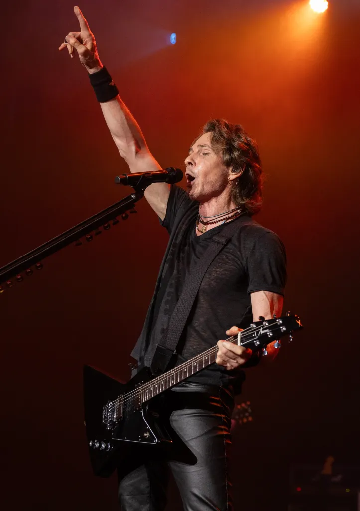 Rick Springfield performing at the Genesee Theatre, playing a black electric guitar and singing into a microphone, with one arm raised.