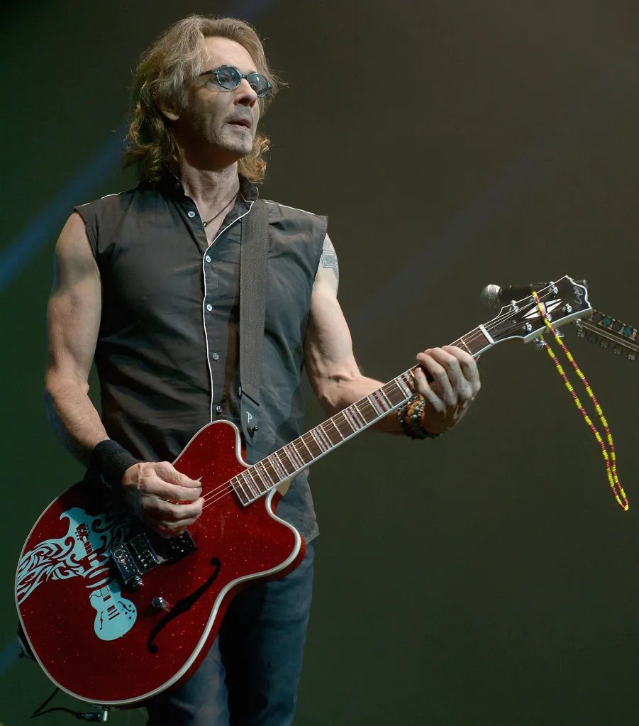 Rick Springfield performing live on stage with a red electric guitar.