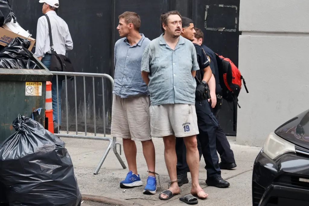Two handcuffed men, Andrew Truelove and another, stand on a street next to police officers after being arrested at Rockefeller Center studios.