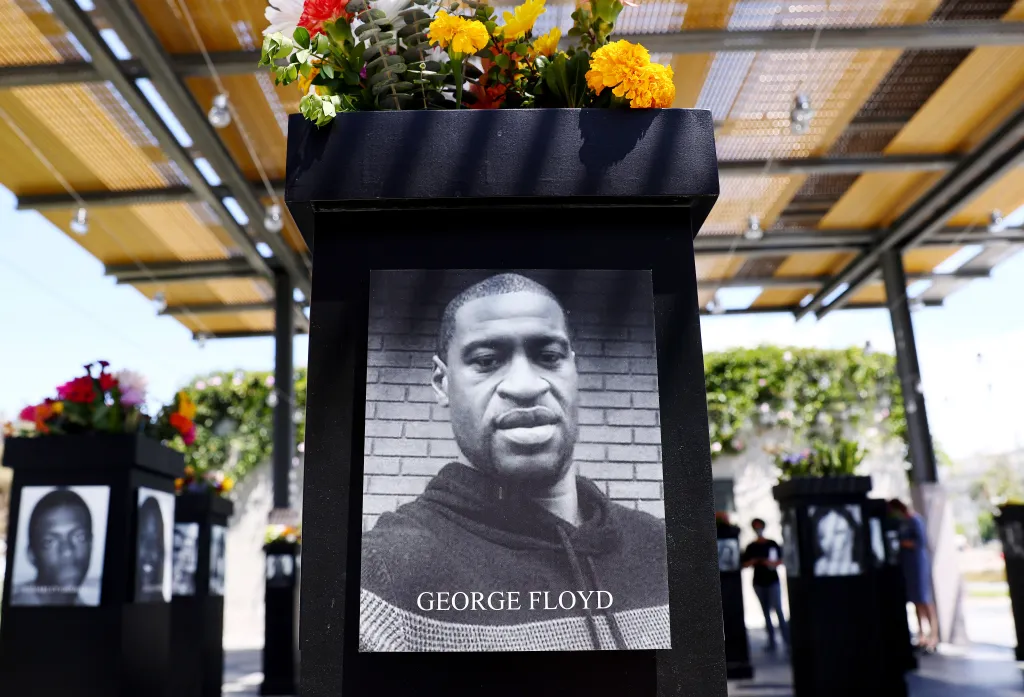 A photograph of George Floyd is displayed on a memorial, featuring his name at the bottom.