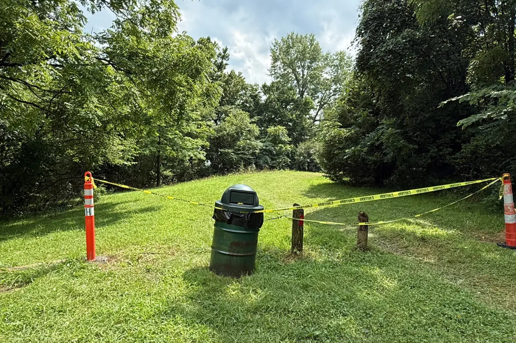 A section of the Riverside Dr Scioto Fishing Area in Powell, Ohio, sectioned off by yellow caution tape stretched between two orange traffic cones and a green trash can.