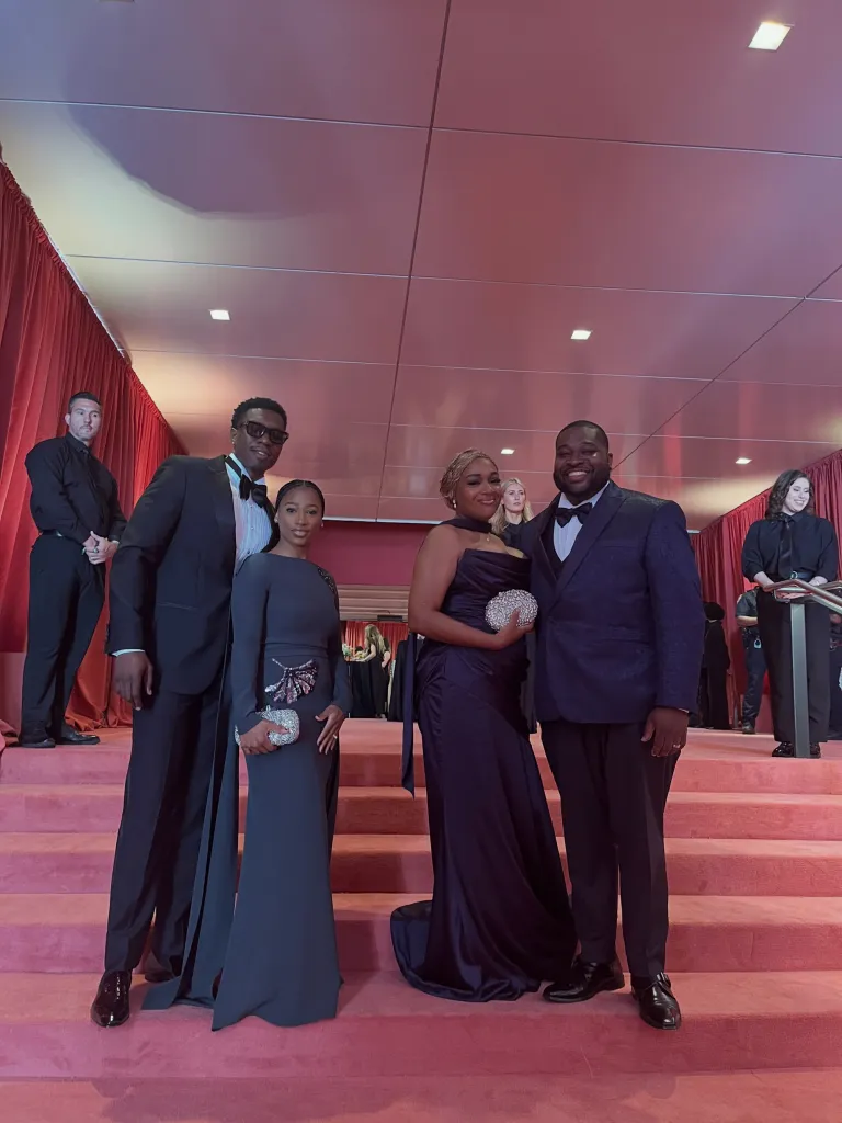 Four guests dressed in formal evening wear on a red carpet.